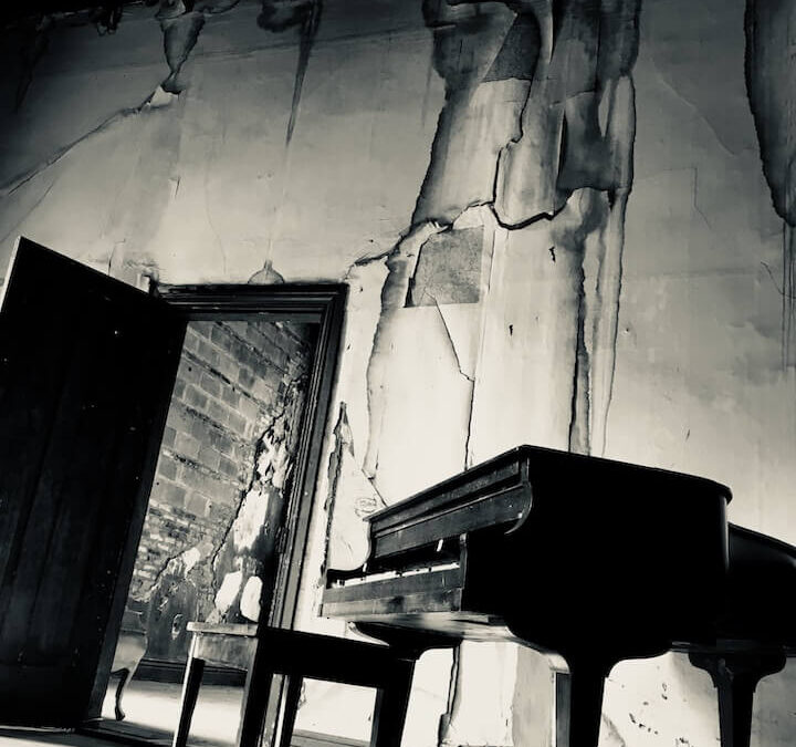 Distressed room with an open door and dilapidated ceiling and walls. Piano is room