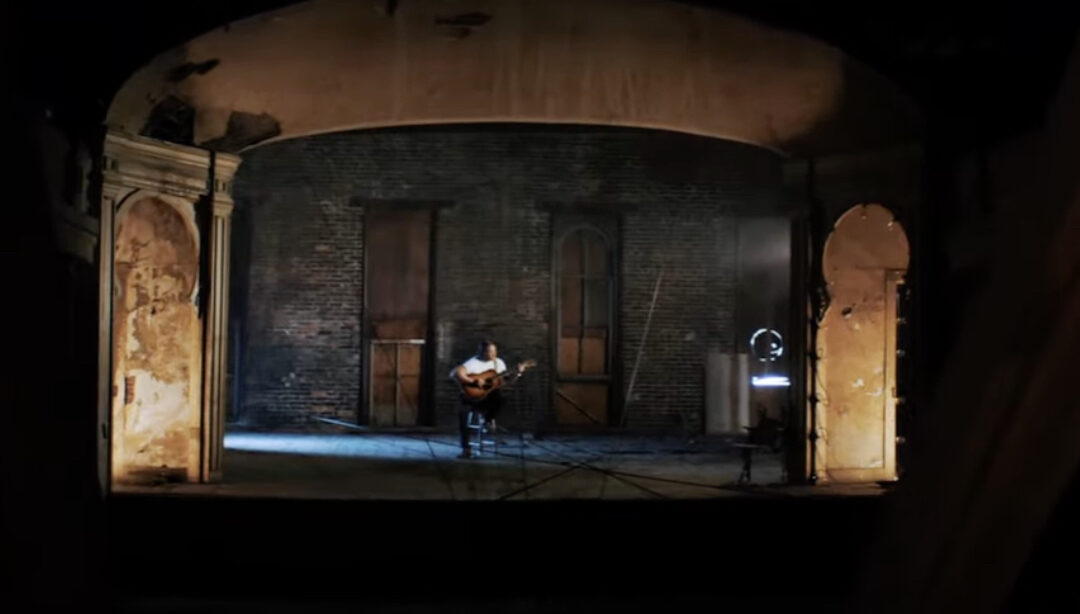 Billy Dawson sitting and playing guitar on Antoinette Hall stage on set on music video, "Before You Go."